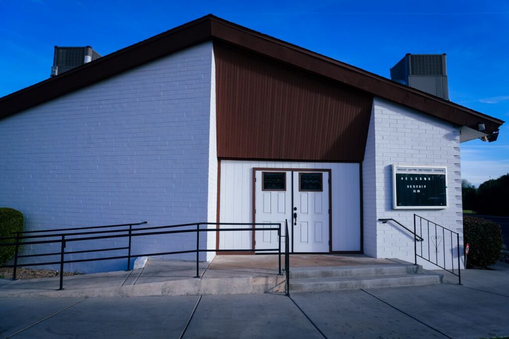 Charming small church entrance with white brick facade under a clear blue sky.